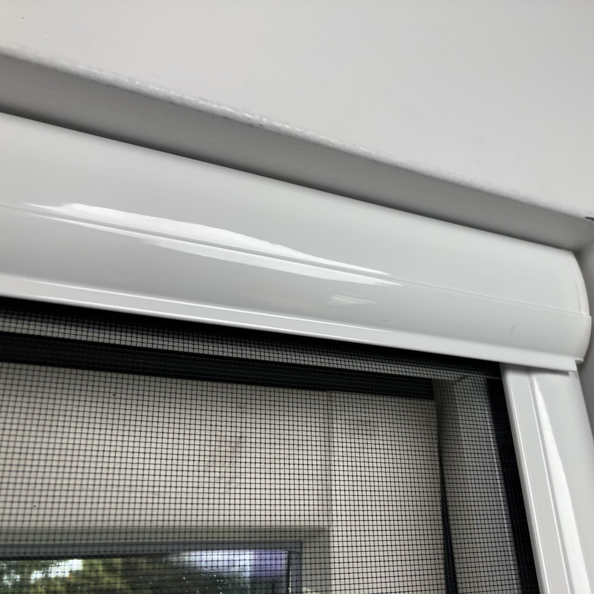 Baltā loga rāmis ar sieta sietu, kas novietots pie baltas sienas, tuvplānā.