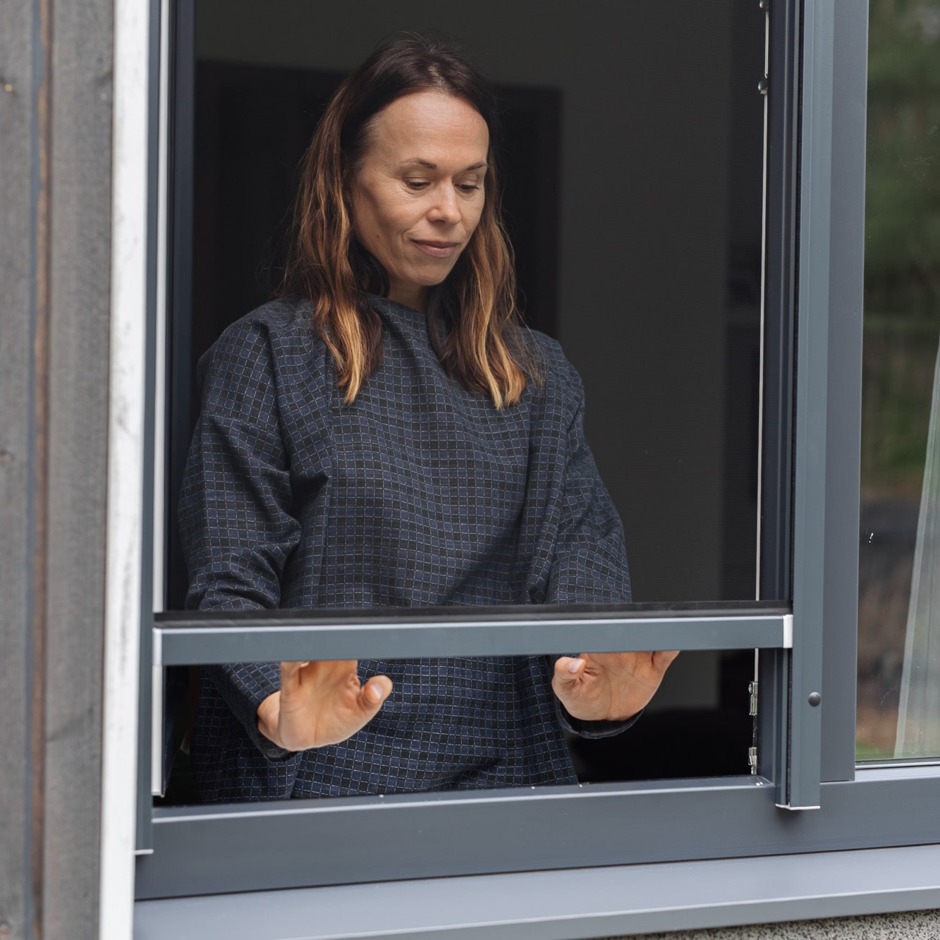 Nainen avaa sisätiloissa ikkunan molemmin käsin, jossa on Hyttysverkko ikkunaan - rullaverkko.