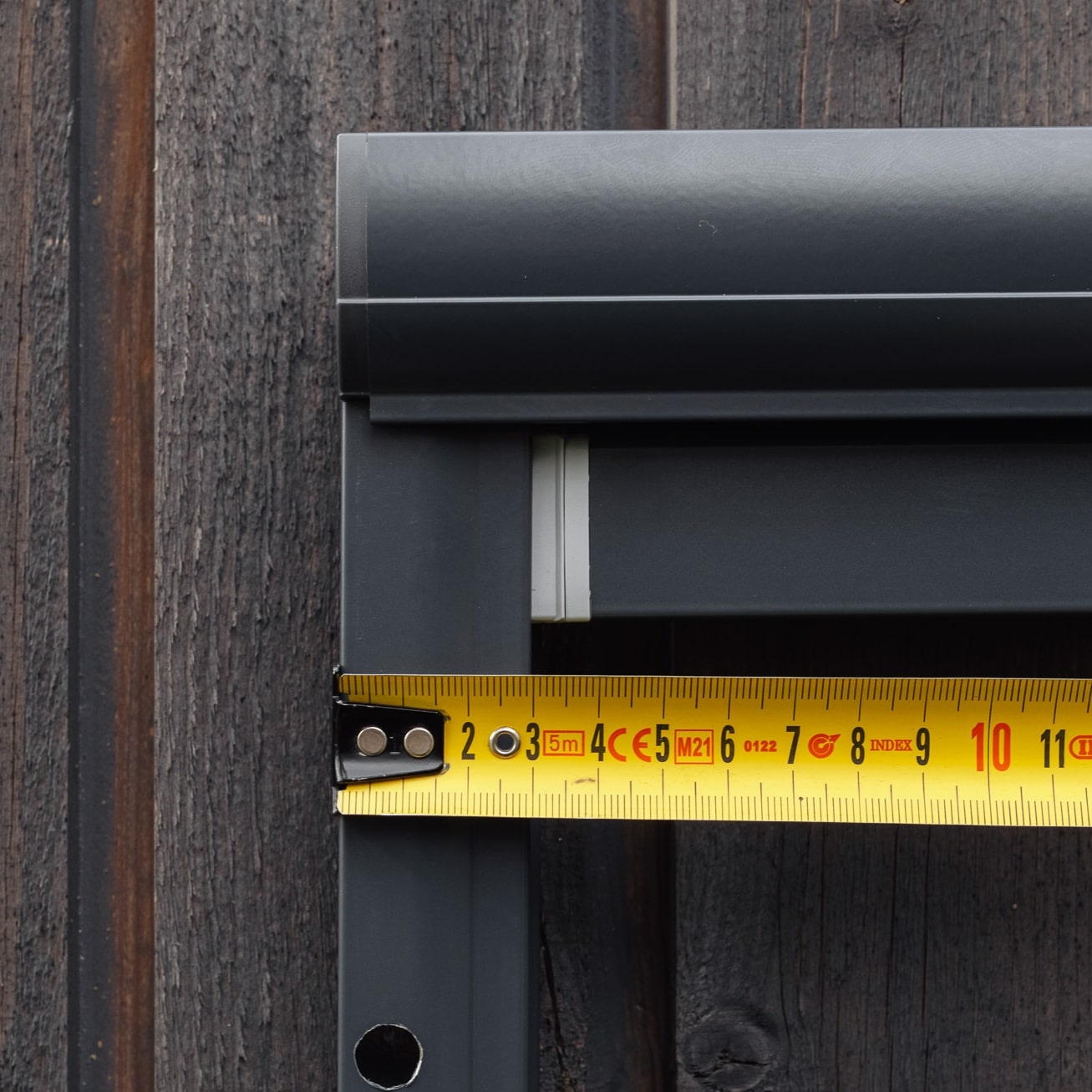 Mittanauhaa pidetään harmaata kehystä vasten Hyttysverkko ikkunaan - rullaverkko on asennettu puuseinälle.