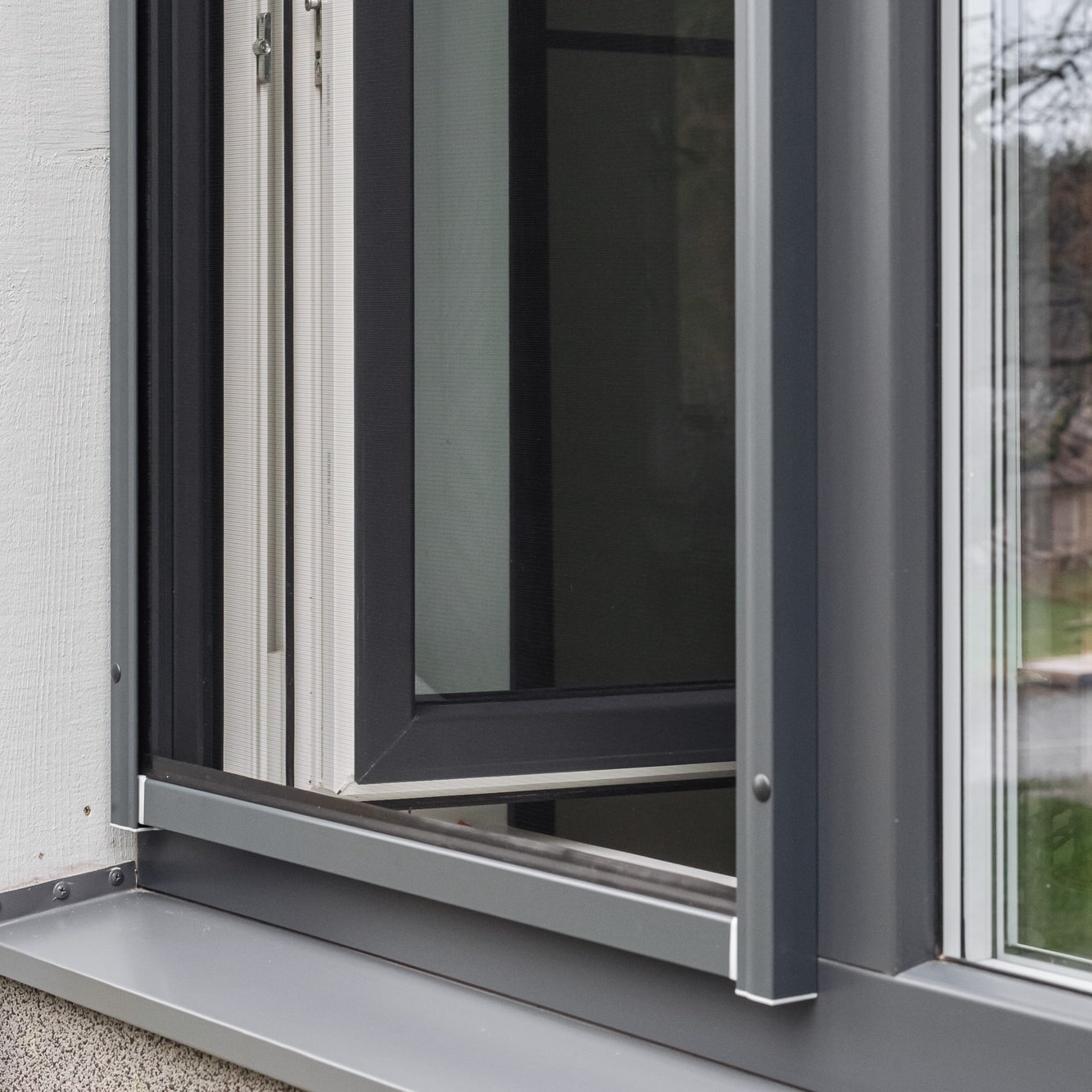 Lähikuva modernista ikkunasta, jossa on metallikehys ja Hyttysverkko ikkunaan - rullaverkko, jossa näkyy sarana ja seinän yksityiskohta.