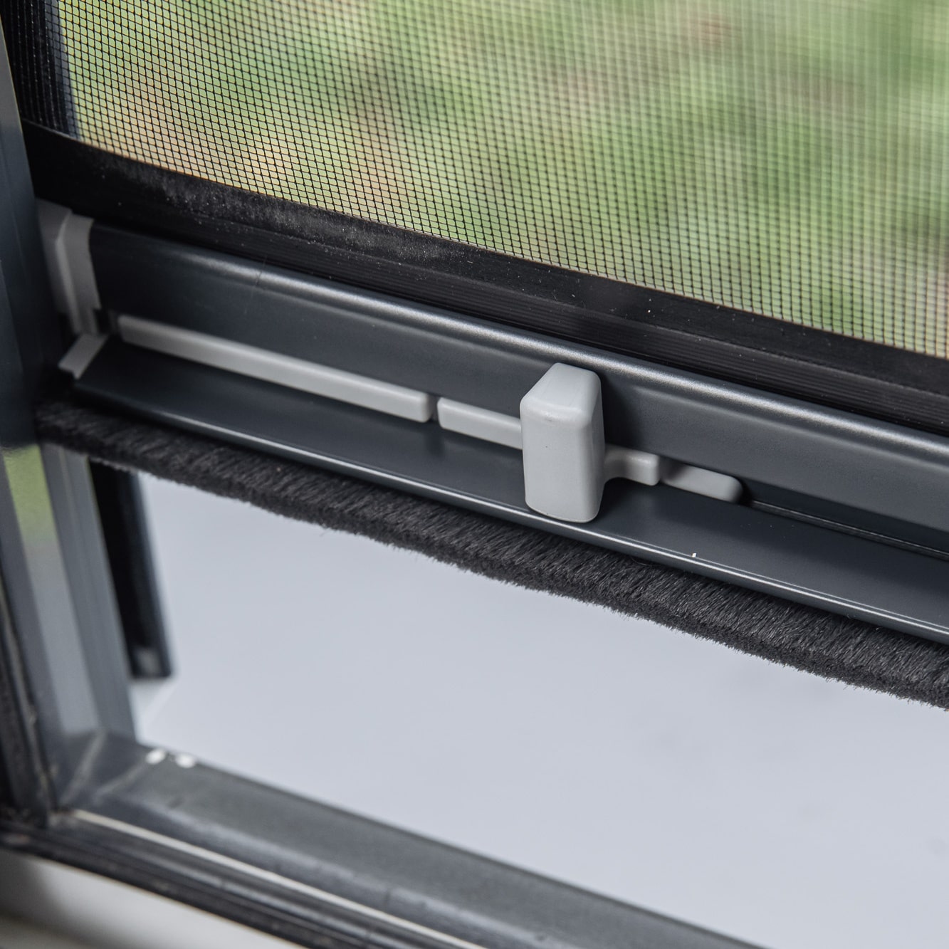 Lähikuva Hyttysverkko ikkunaan - rullaverkko harmaalla salvalla, mustalla sääsuojalla ja lisätyllä hyönteissuojalla.