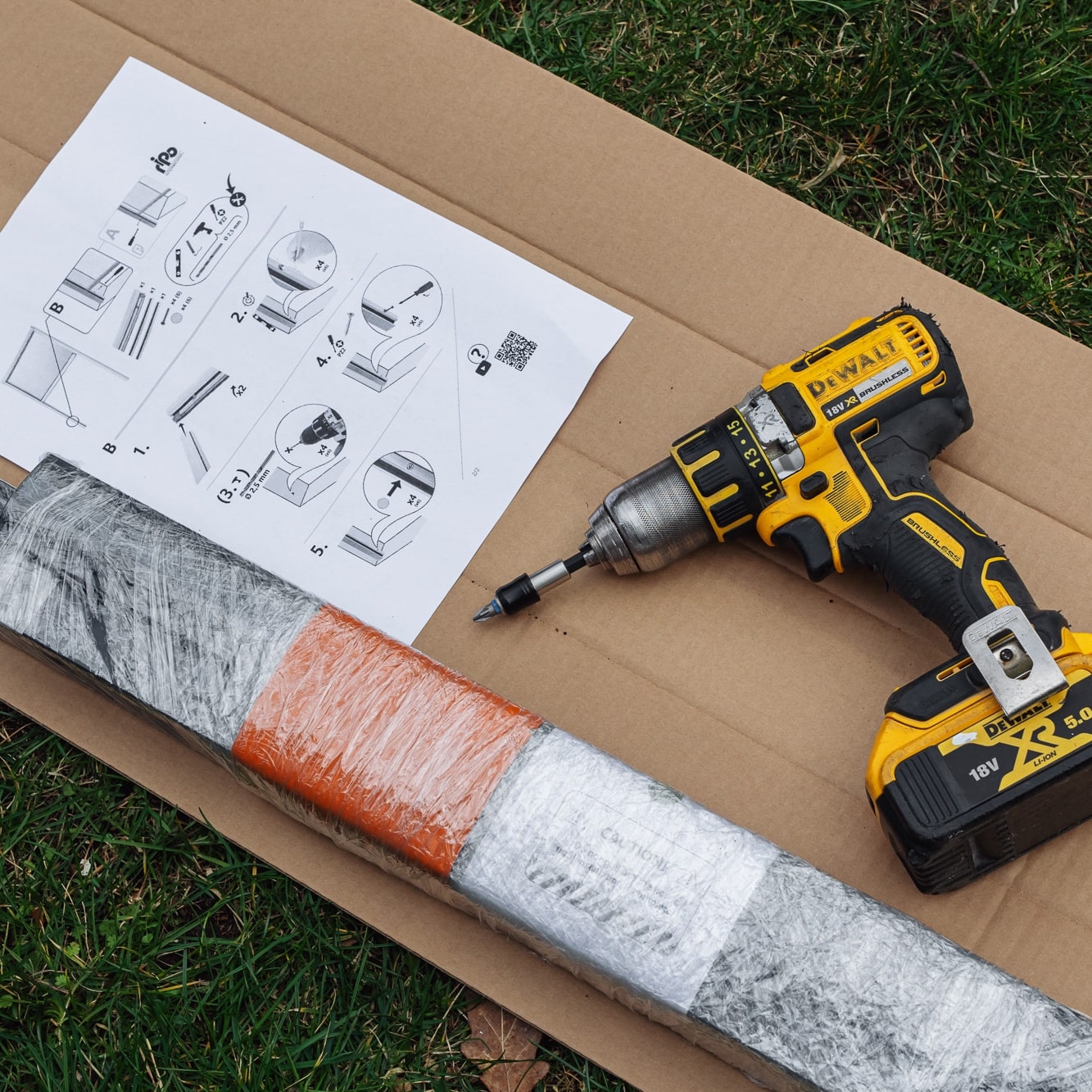 Hyttysverkko ikkunaan - rullaverkko, kääritty metalliosa ja ohjeet sijoitettu pahville ruohon päälle.