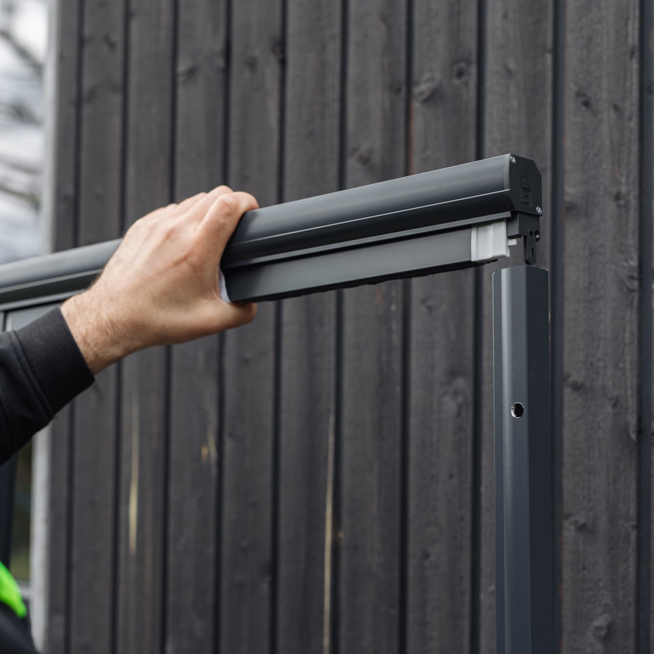 Joku asentaa Hyttysverkko ikkunaan - rullaverkko kehyksen tummaa puuseinää vasten.