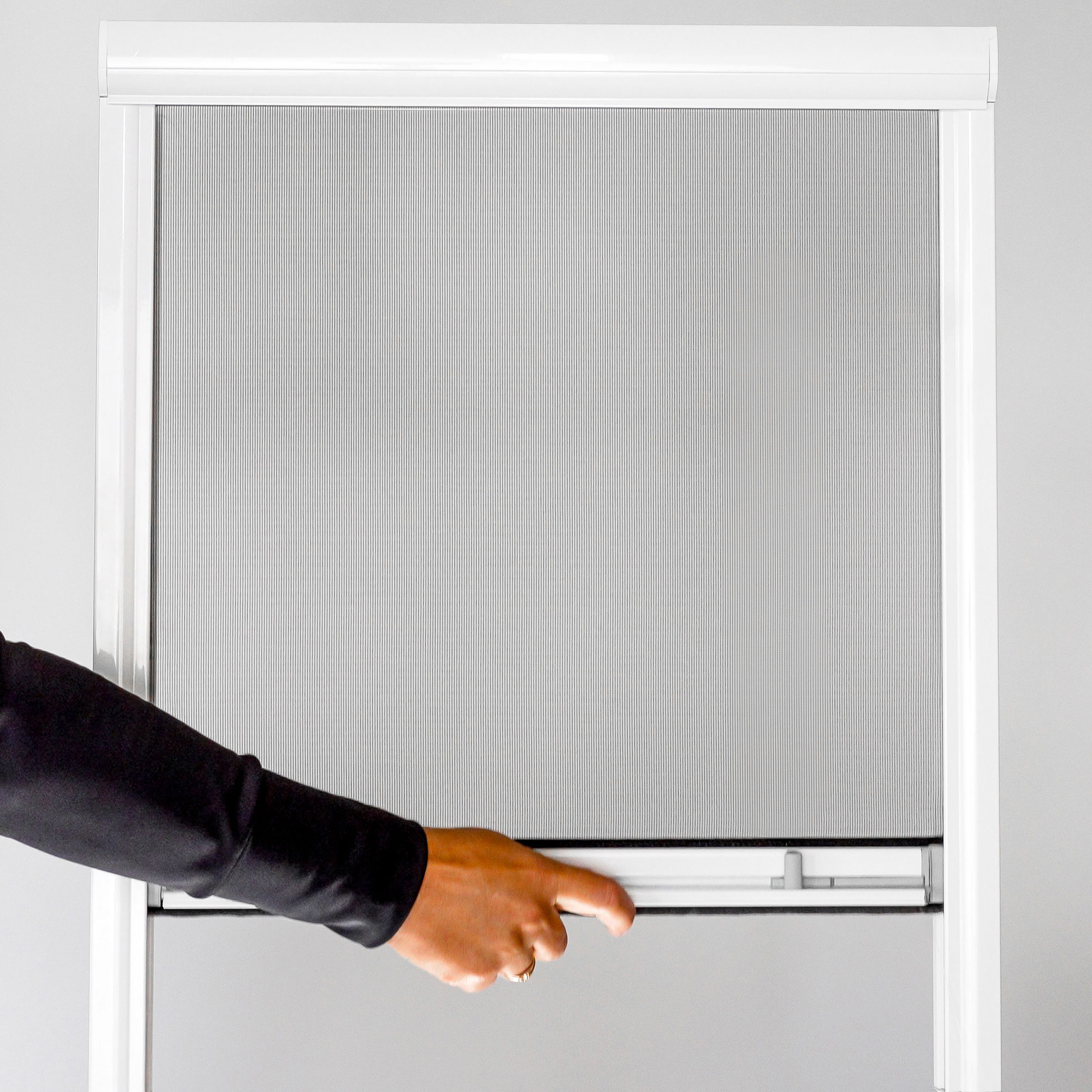 Käsi vetää alas Hyttysverkko ikkunaan - rullaverkko ikkunaseinää vaaleaa taustaa vasten.