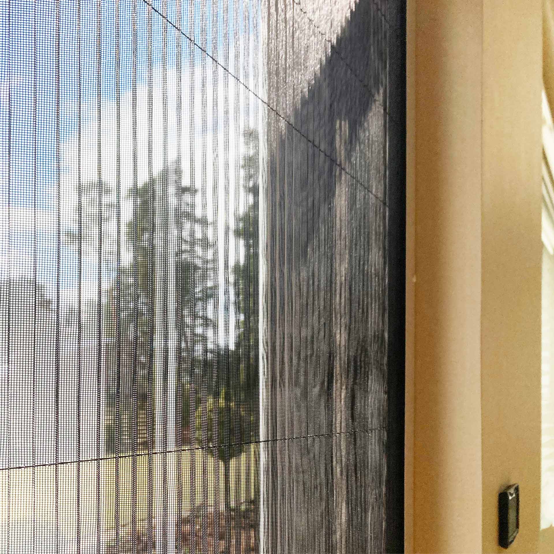 Blick durch eine Fliegengitter Tür - faltbar mit Bäumen im Freien, mit einem Teil einer Innenwand und einem elektronischen Schalter im Blick.