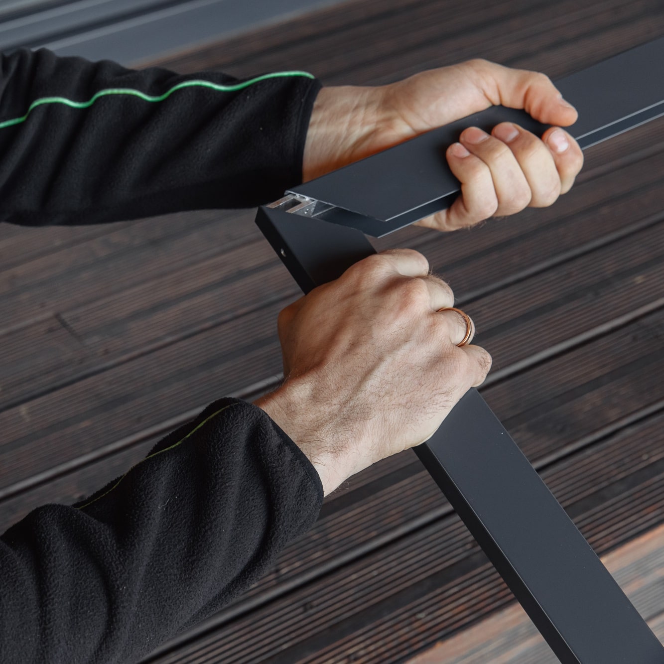 Henkilö kokoaa puulattialla kahta Hyttysverkko oveen - taitettava metallista runkopalaa, yksi osa kummassakin kädessä.